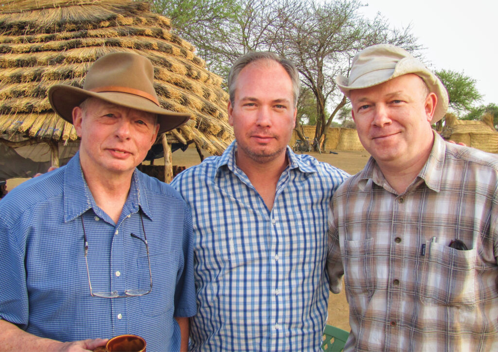 Three men standing together outside in a village